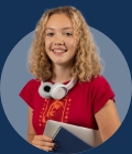 Sixth form student smiling and holding a notebook on a grey background.